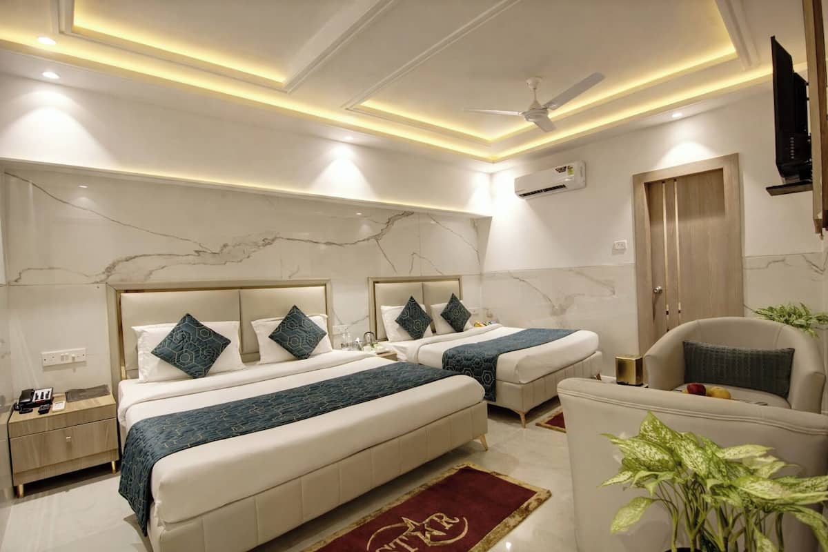 A hotel room with two beds, a ceiling fan, an air conditioning unit, a TV, a desk, and a chair.
