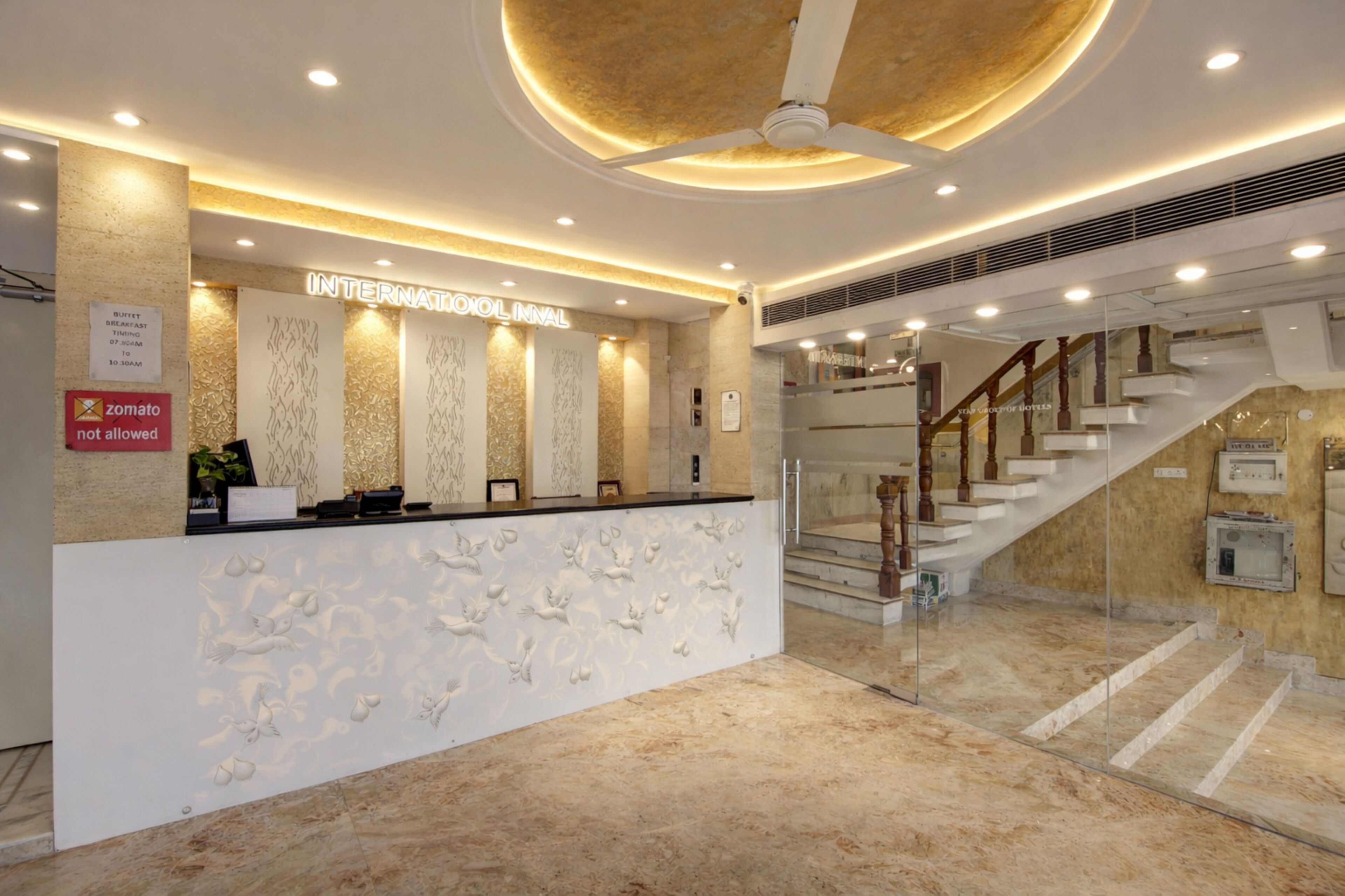 Ein Hotel-Empfangsbereich mit modernem Design, einer Rezeption, einer Treppe und einem Deckenventilator.