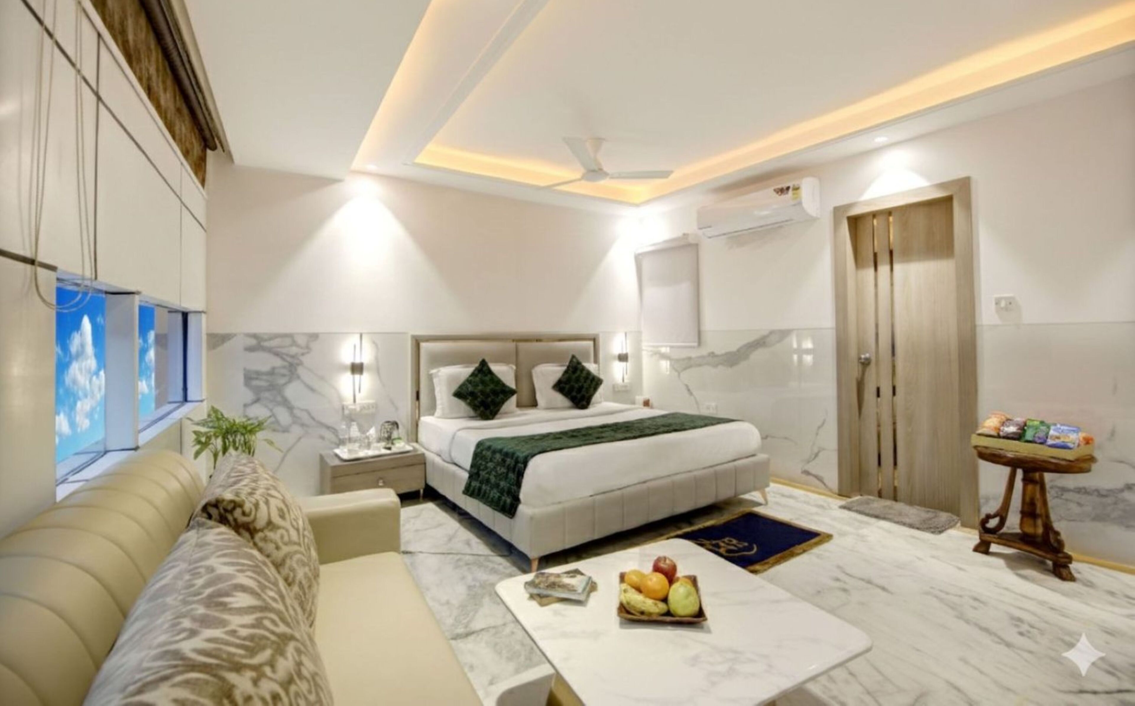 Une chambre d’hôtel moderne équipée d’un lit, d’un canapé, d’une table de chevet avec des fruits, d’une petite table avec des en-cas et d’un ventilateur de plafond.