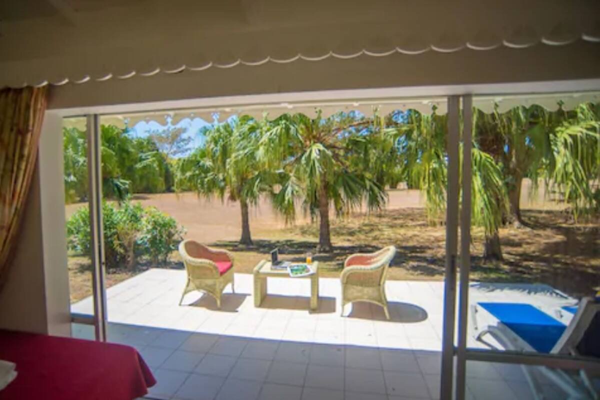 A room with a large sliding glass door leading to an outdoor area with two wicker chairs, a small table, and a pool.