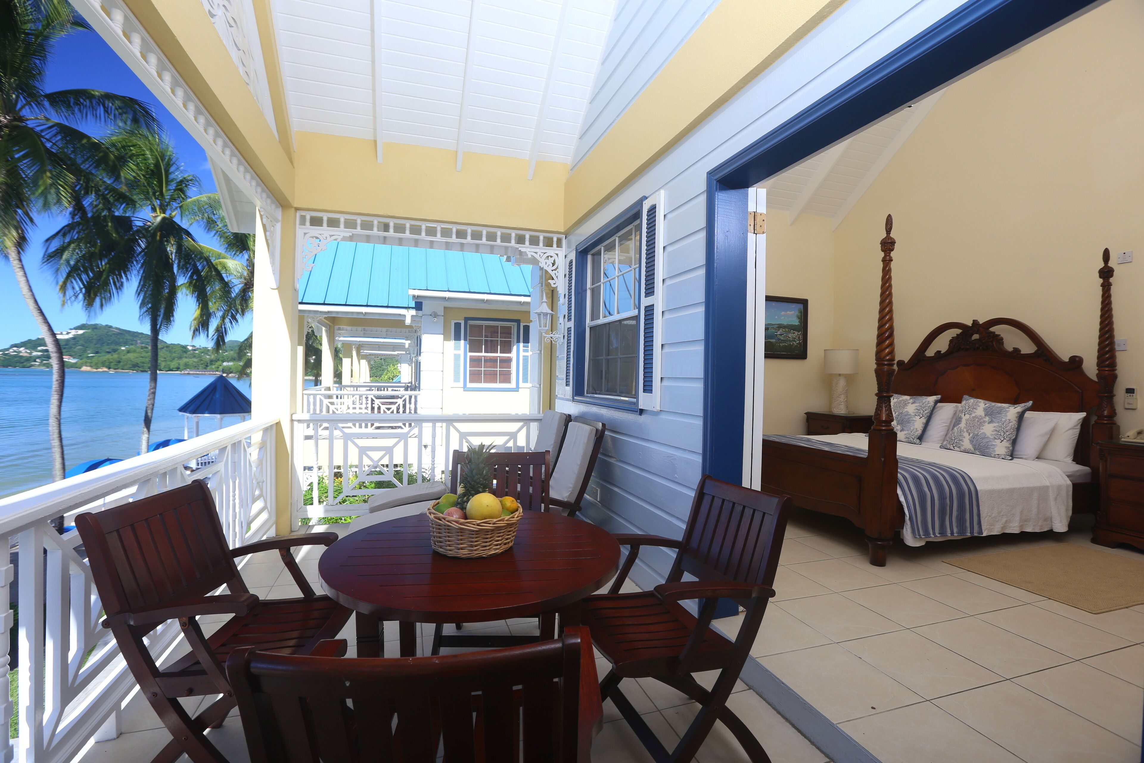 A balcony with a wooden table and chairs, a bed with a wooden headboard, and a view of the sea.