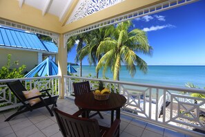 A balcony with a view of the ocean, a table with chairs, and a basket of fruit. - Villa Beach Cottages (Castries)