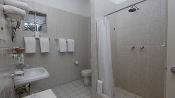 Baño con lavamanos, inodoro y ducha. Varias toallas cuelgan de un perchero.