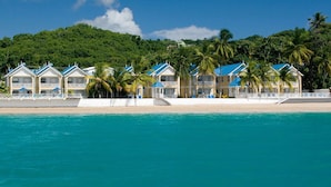Un hotel frente a la playa con varios edificios de techos azules, una playa de arena y palmeras.
