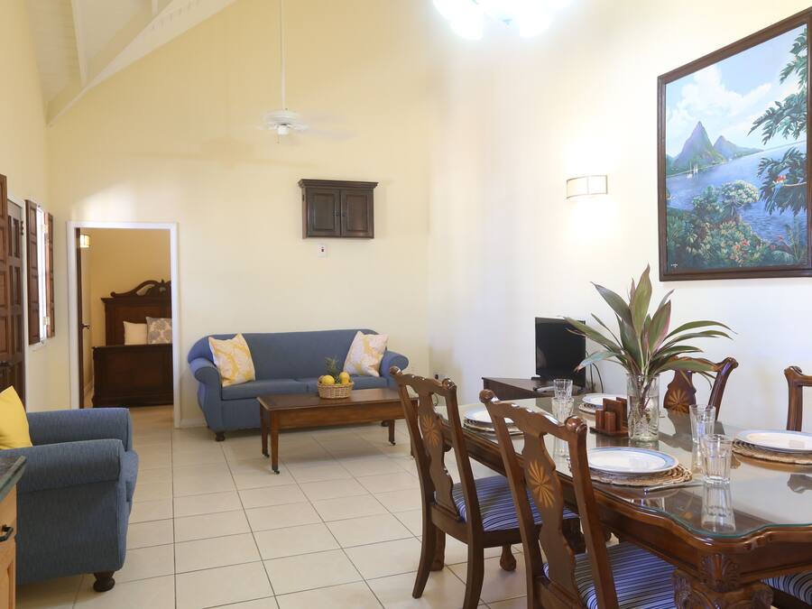 A living room with a blue sofa, a dining table set for two, and a large framed picture on the wall.