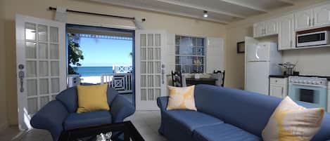 A living room with a blue sofa, yellow cushions, a ceiling fan, and a view of the ocean through a sliding door.