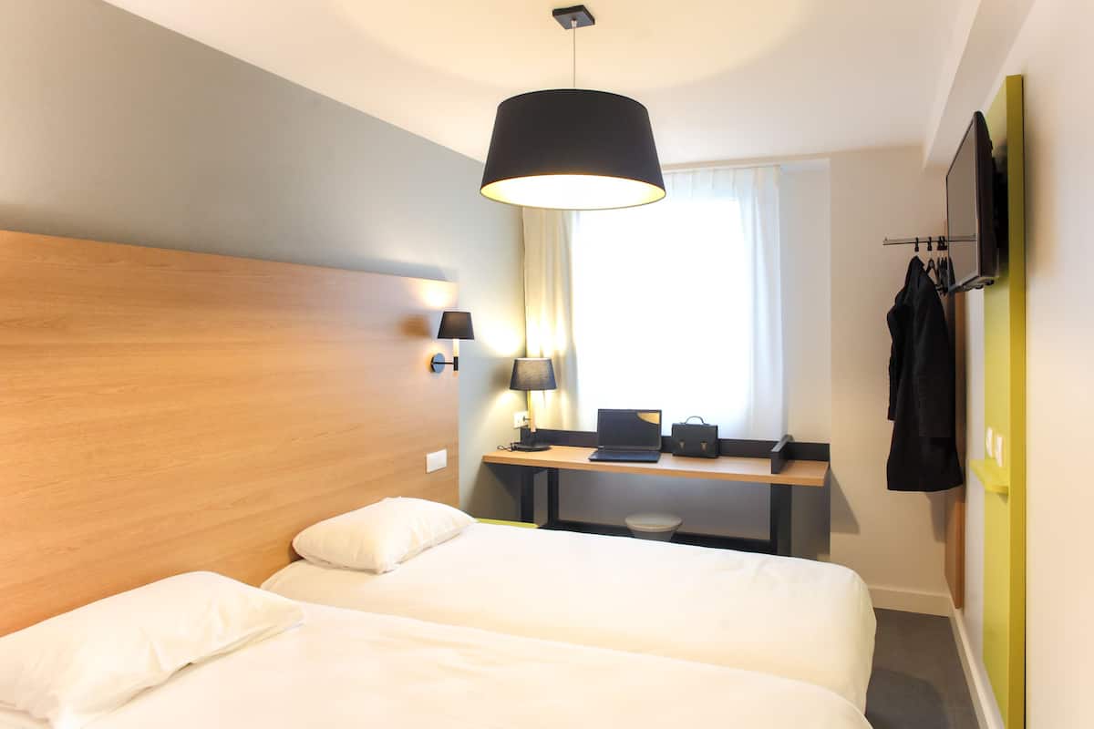 Habitación de hotel con cama doble, escritorio con computadora portátil, lámpara y televisor montado en la pared.