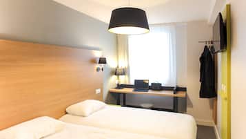 Habitación de hotel con cama doble, escritorio con computadora portátil, lámpara y televisor montado en la pared.