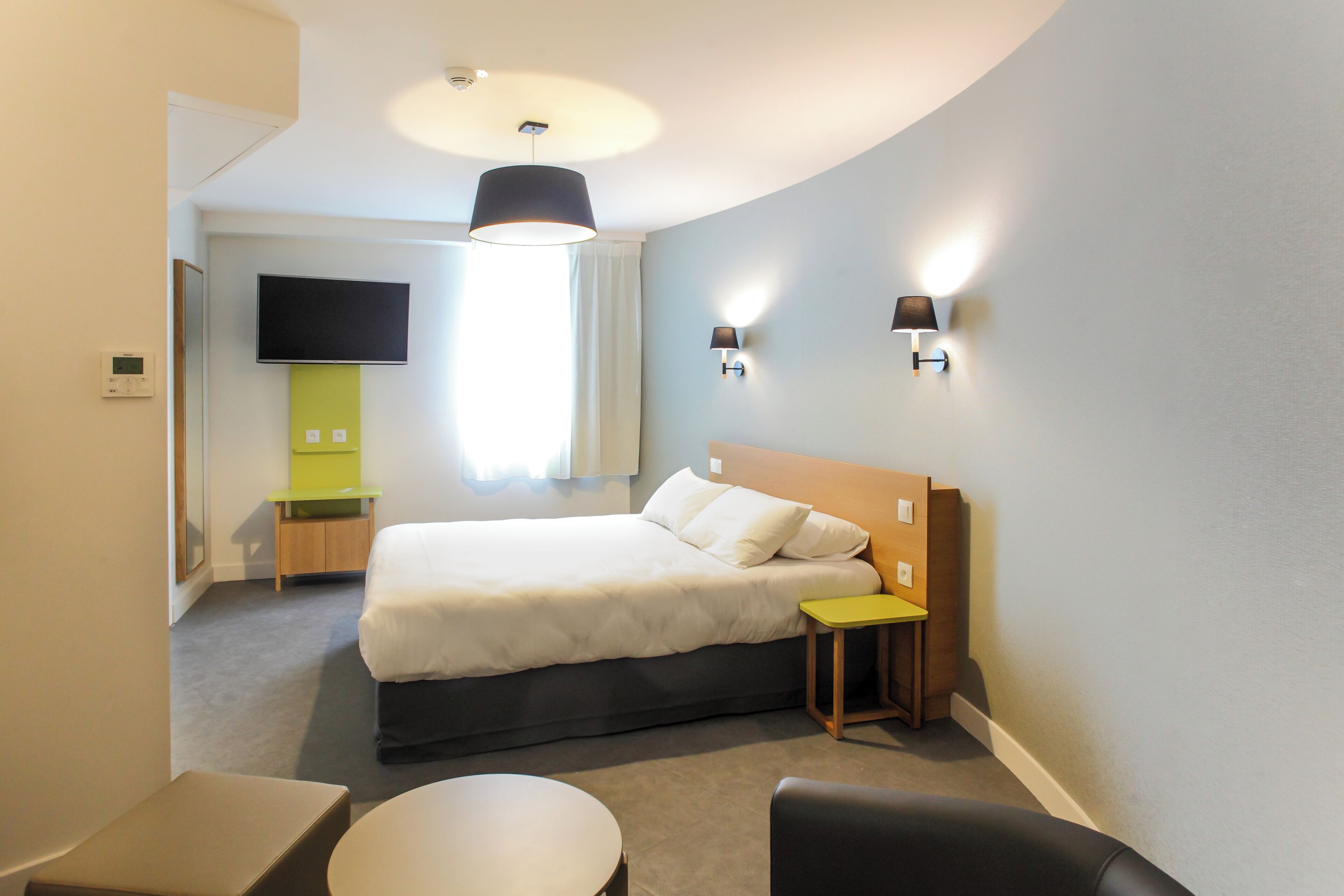 Ein Hotelzimmer mit einem Bett, einem Schreibtisch, einem Sessel, einem Fernseher und einer Lampe.