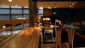 Un espace bar doté d’un comptoir en bois, d’une cloison en verre et d’un réfrigérateur rempli de boissons.