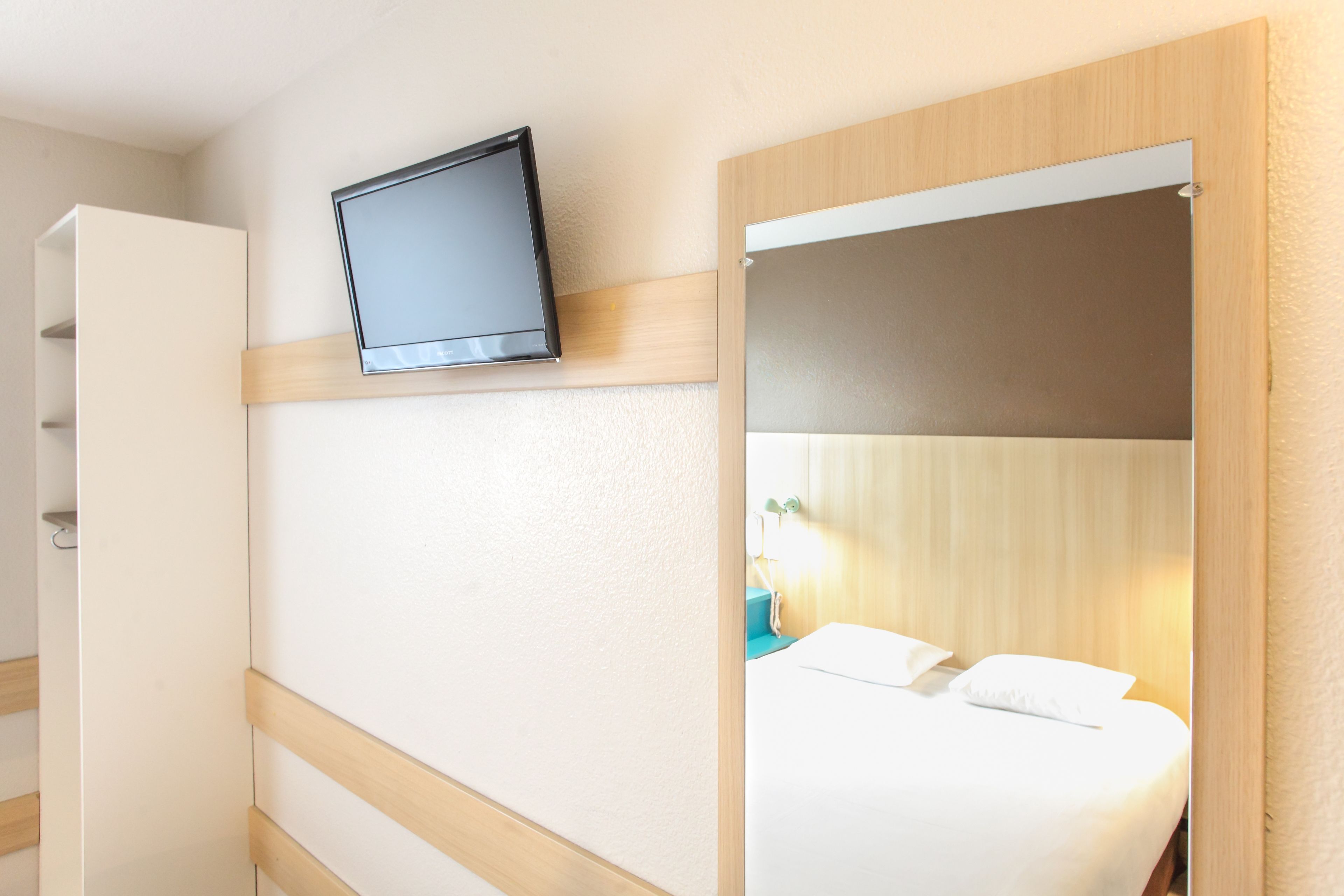 Una habitación de hotel con cama, televisión montada en la pared y armario.