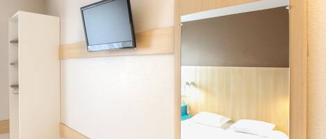 A hotel room with a bed, a television mounted on the wall, and a wardrobe.