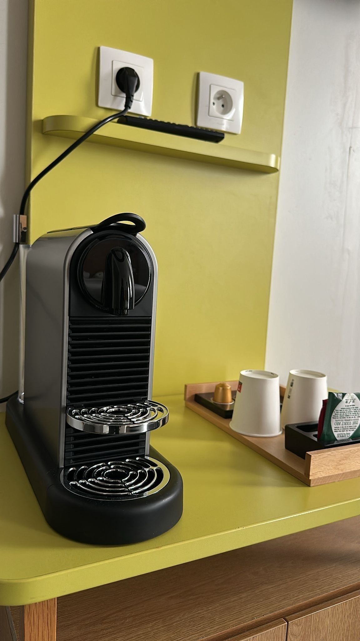 Una macchina per caffè su un piano di lavoro giallo, con una presa di corrente sopra.