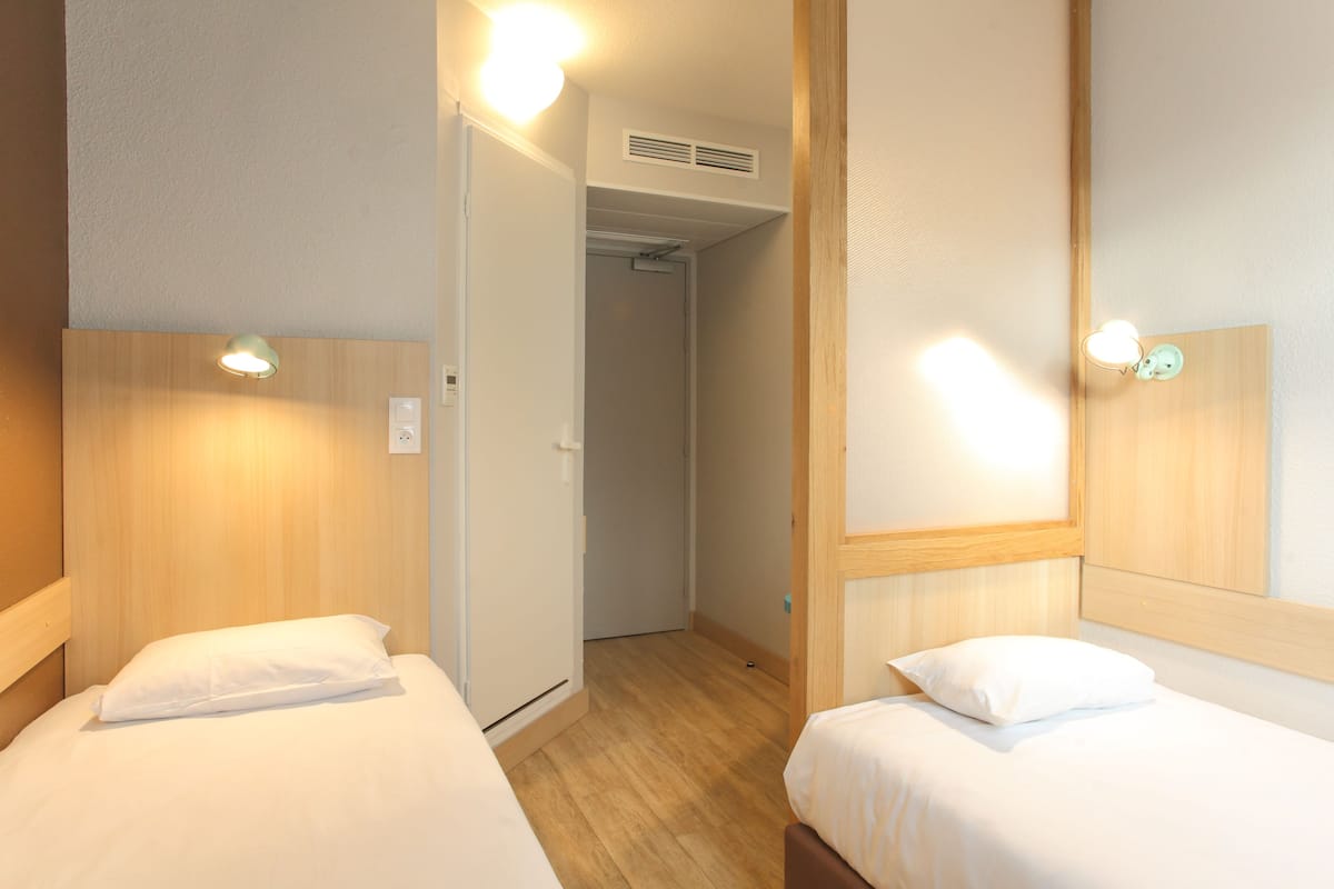 Habitación de hotel con dos camas, cabeceras de madera y lámparas de noche.
