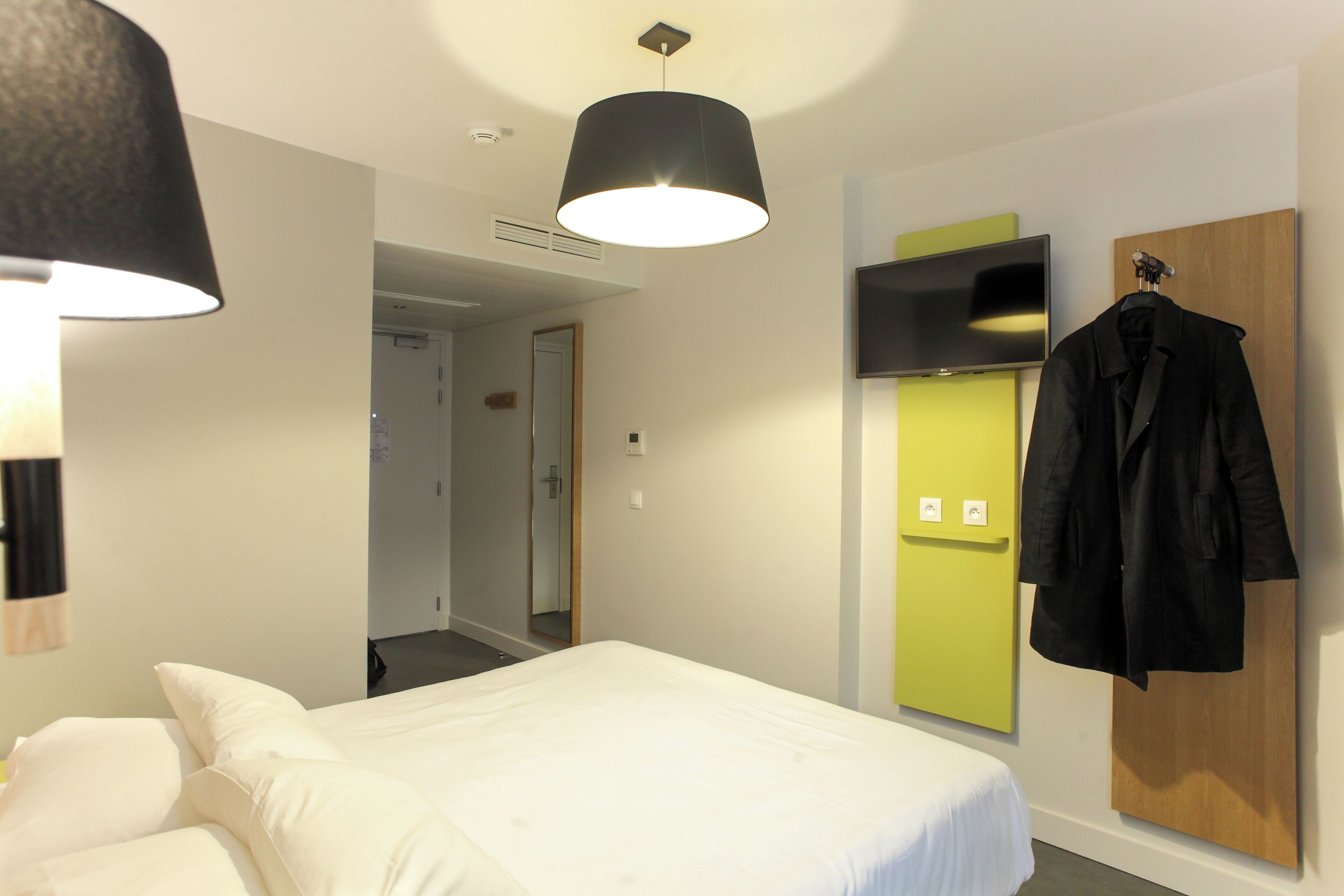 Ein Hotelzimmer mit einem Bett, einem Kleiderhaken, einem Fernseher und einer Tür zu einem anderen Raum.
