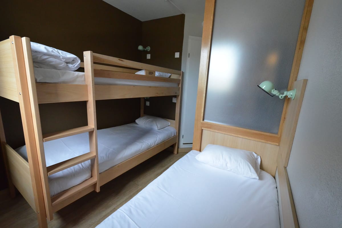 Habitación con literas, un cabecero de madera, una cama individual y una ventana pequeña con cortina.