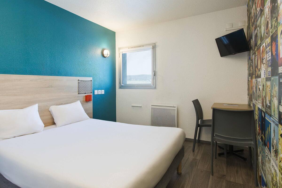 Ein Hotelzimmer mit Bett, Schreibtisch, Stuhl, Fernseher, Fenster und einer Wand mit Postern.