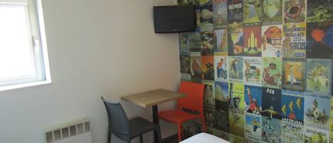 A room with a bed, a table, two chairs, a wall-mounted TV, and a window.