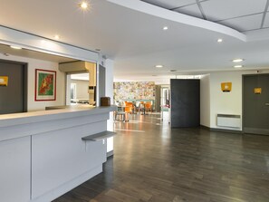 Un hall d’hôtel moderne comprenant un comptoir d’accueil, un espace repas et un mur orné d’un collage de photos.