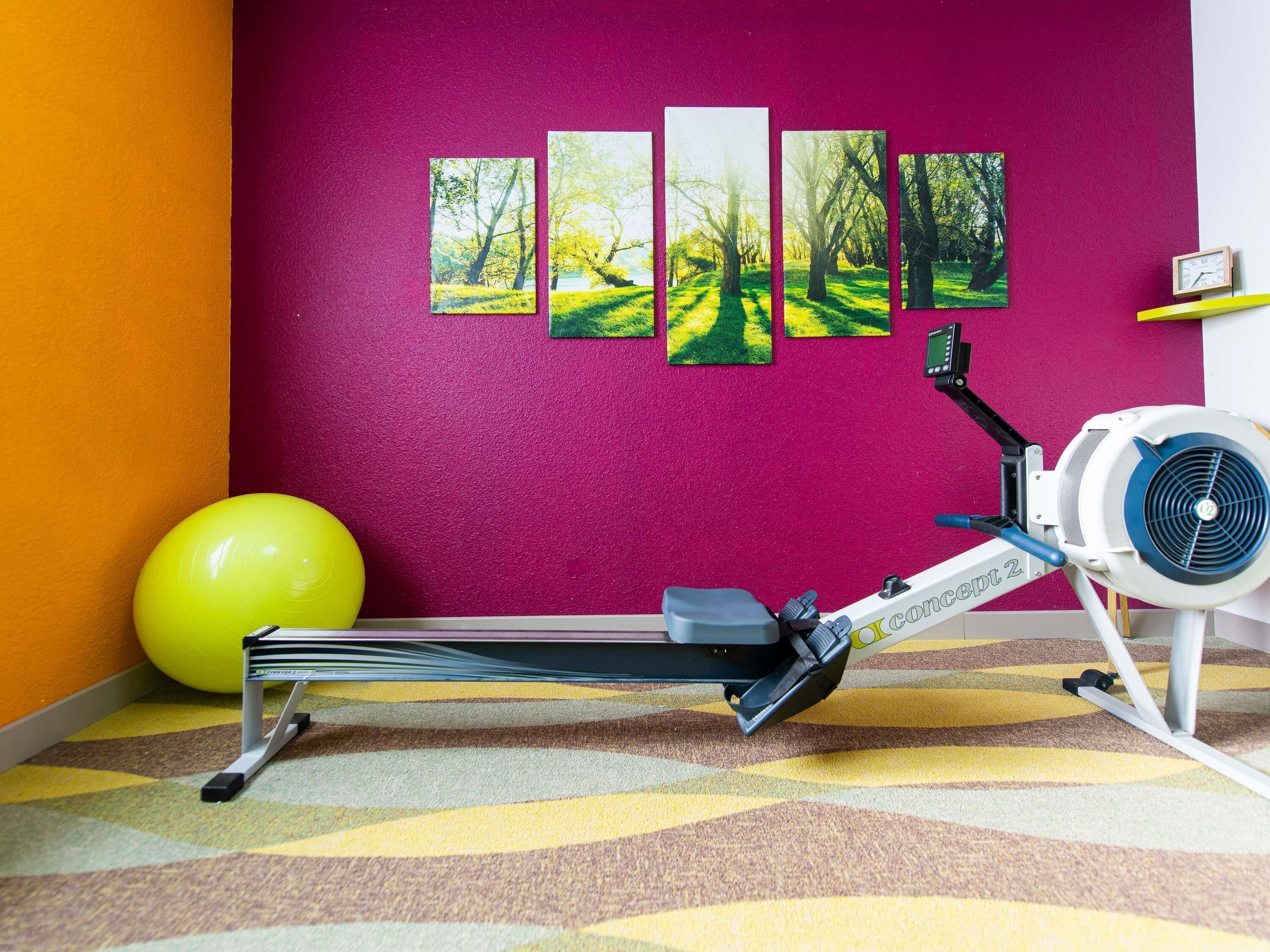 Ein Heimfitnessraum mit einem stationären Fahrrad, einem gelben Trainingsball und einer Wand mit fünf gerahmten Bildern.