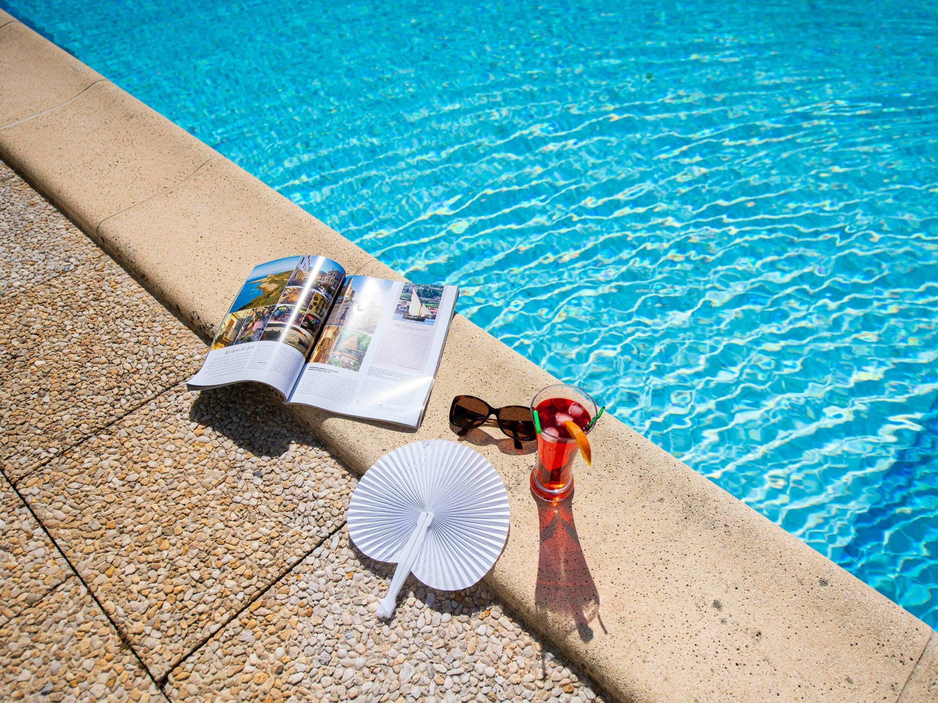 A poolside setting with a book, sunglasses, and a drink.