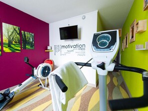 A gym with exercise equipment, motivational posters, and a TV on the wall. - Ibis Styles Gien (Gien)