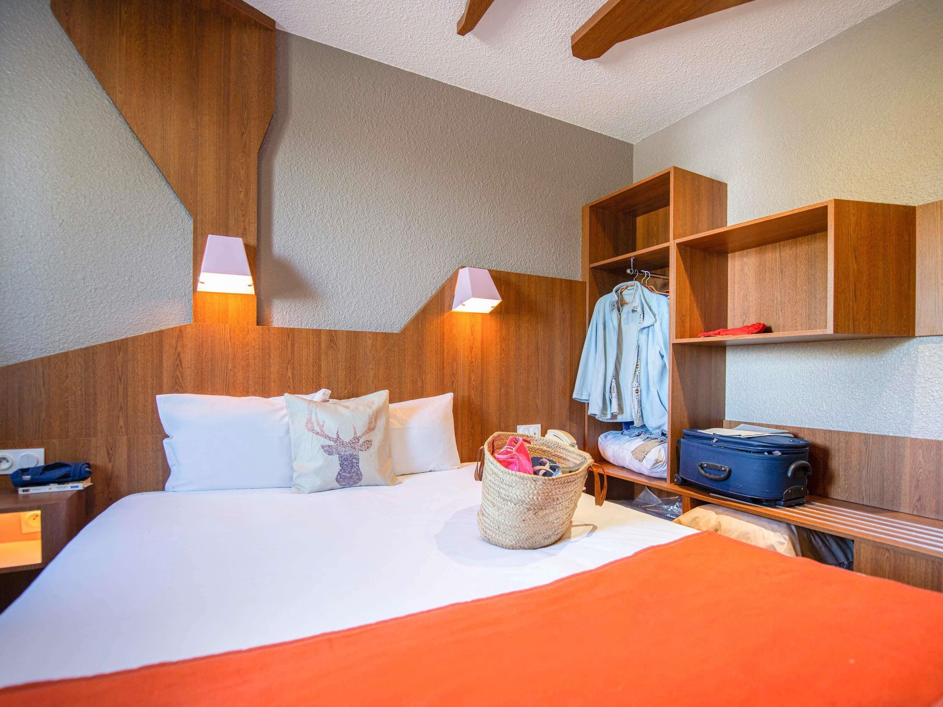 A hotel room with a bed, a bedside table, a lamp, a wardrobe, and a suitcase.