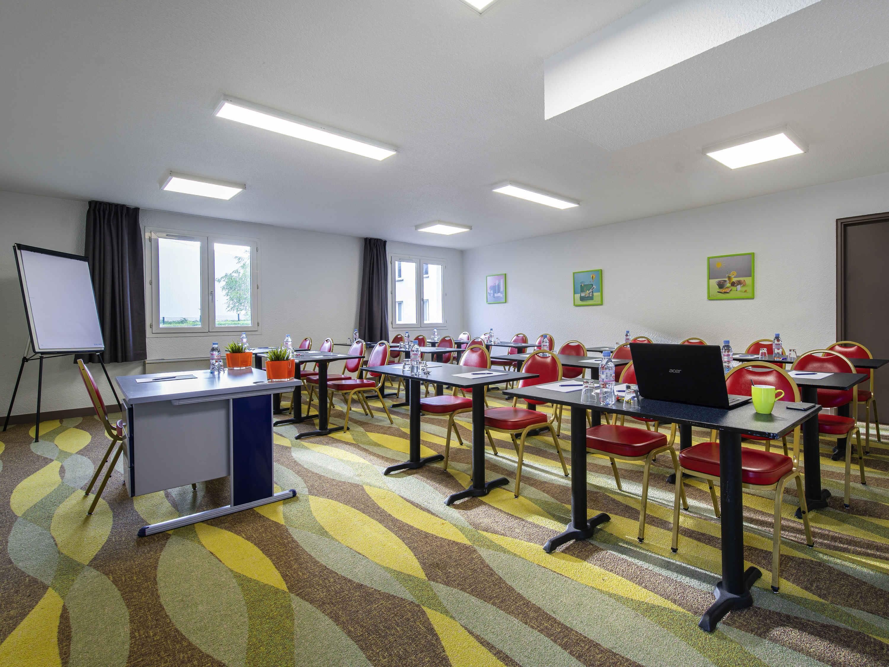 Une salle de conférence équipée de tables, de chaises, d’un tableau blanc et d’un ordinateur portable.