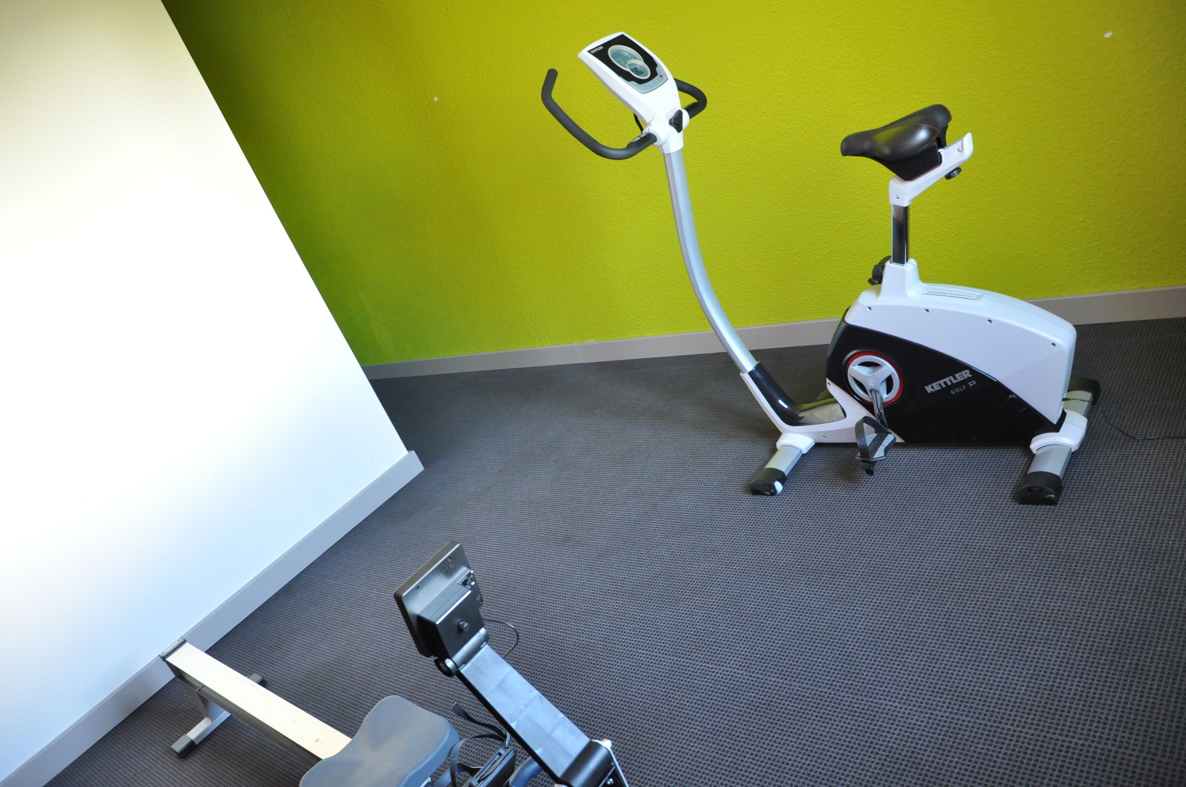An exercise bike in a room with a green wall and carpeted floor.