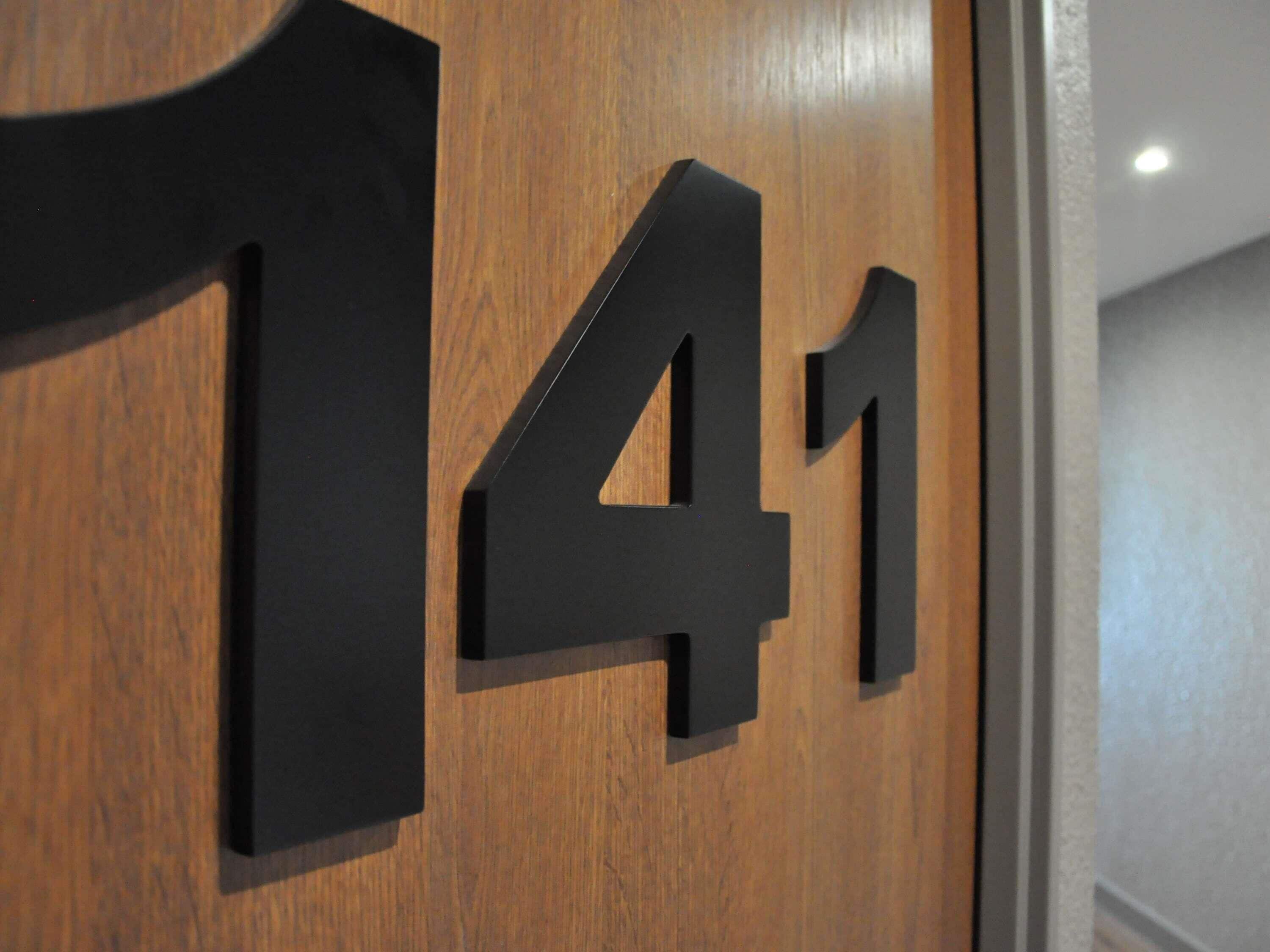 Een houten deur met een zwart naambordje met het nummer 141 erop.