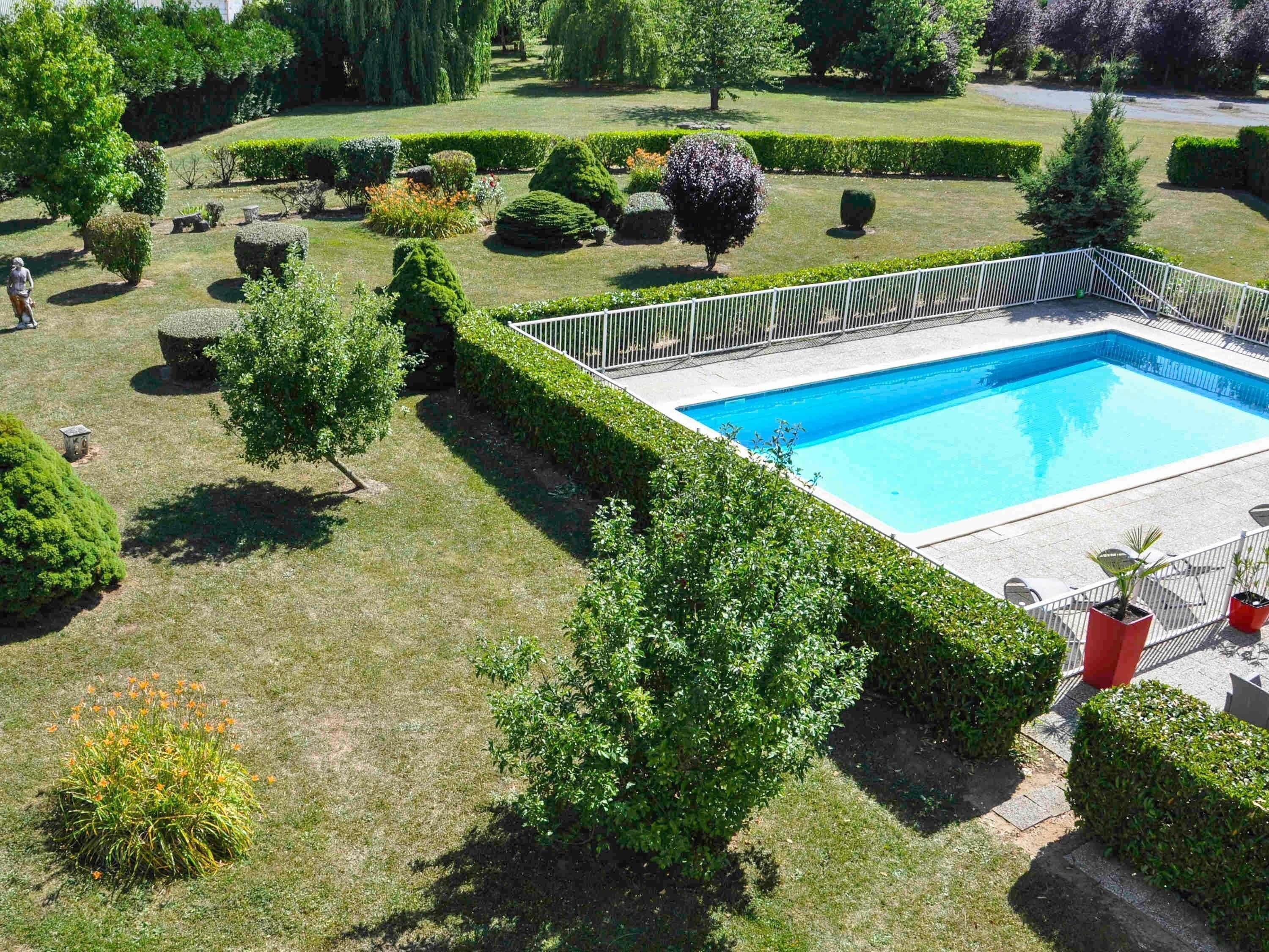 A swimming pool surrounded by neatly trimmed hedges and a variety of trees.