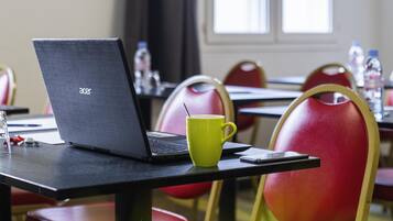 A laptop on a table with a yellow mug, red chairs, and a window in the background.