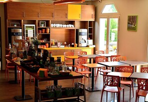 A modern cafe with wooden cabinets, orange chairs, and a variety of kitchen appliances. - Ibis Styles Gien (Gien)