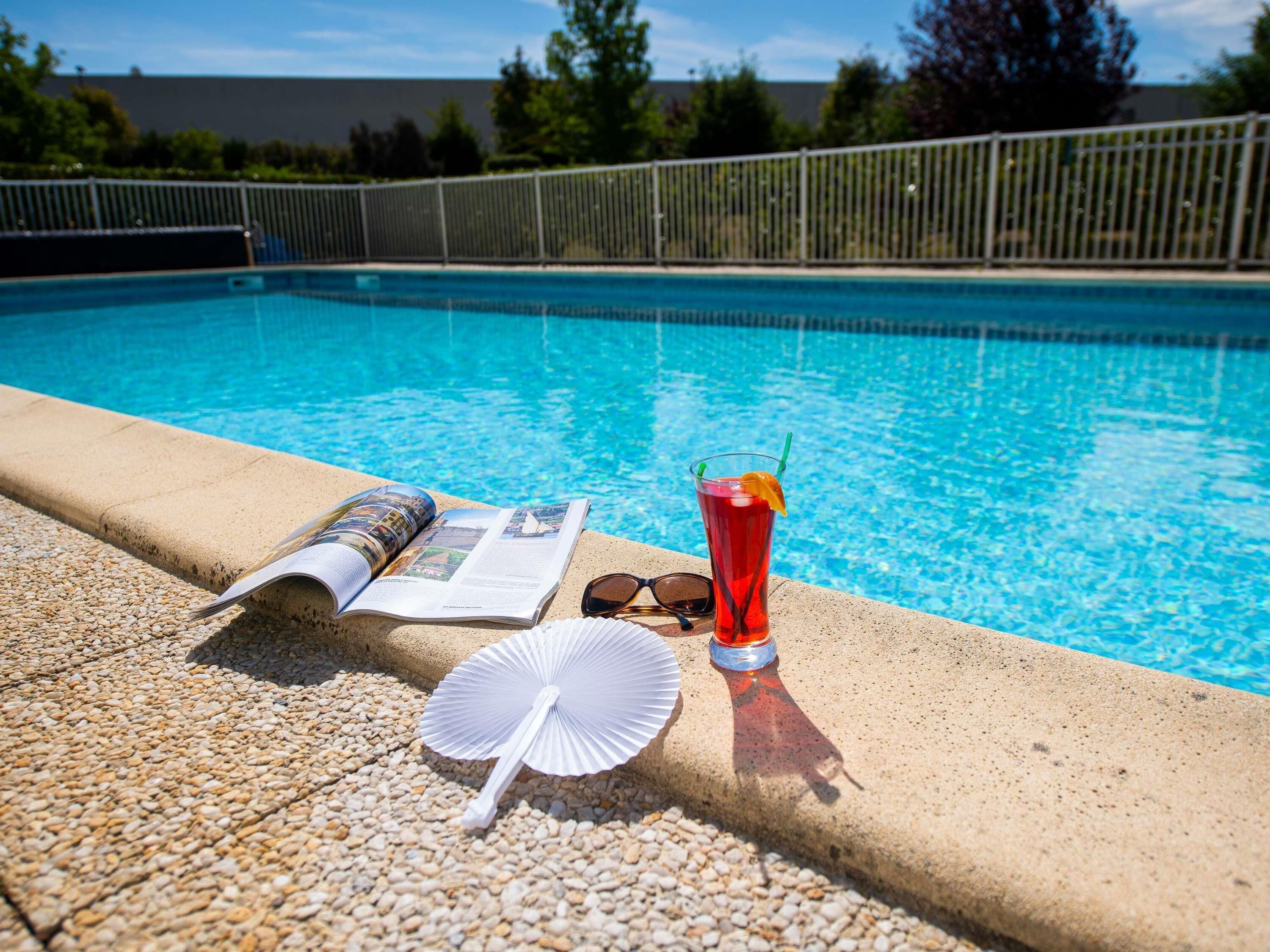 Escena junto a la piscina con una revista, gafas de sol y una bebida.
