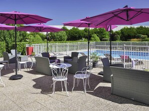 An outdoor seating area with patio furniture, umbrellas, and a pool. - Ibis Styles Gien (Gien)
