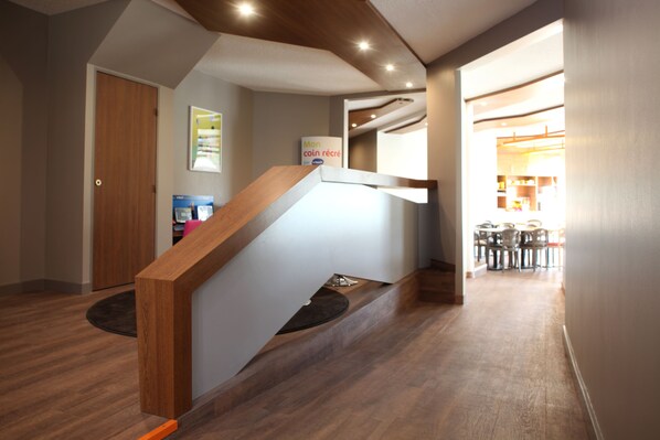 A modern interior with a wooden staircase, a dining area in the background, and a sign on the wall. - Ibis Styles Gien (Gien)