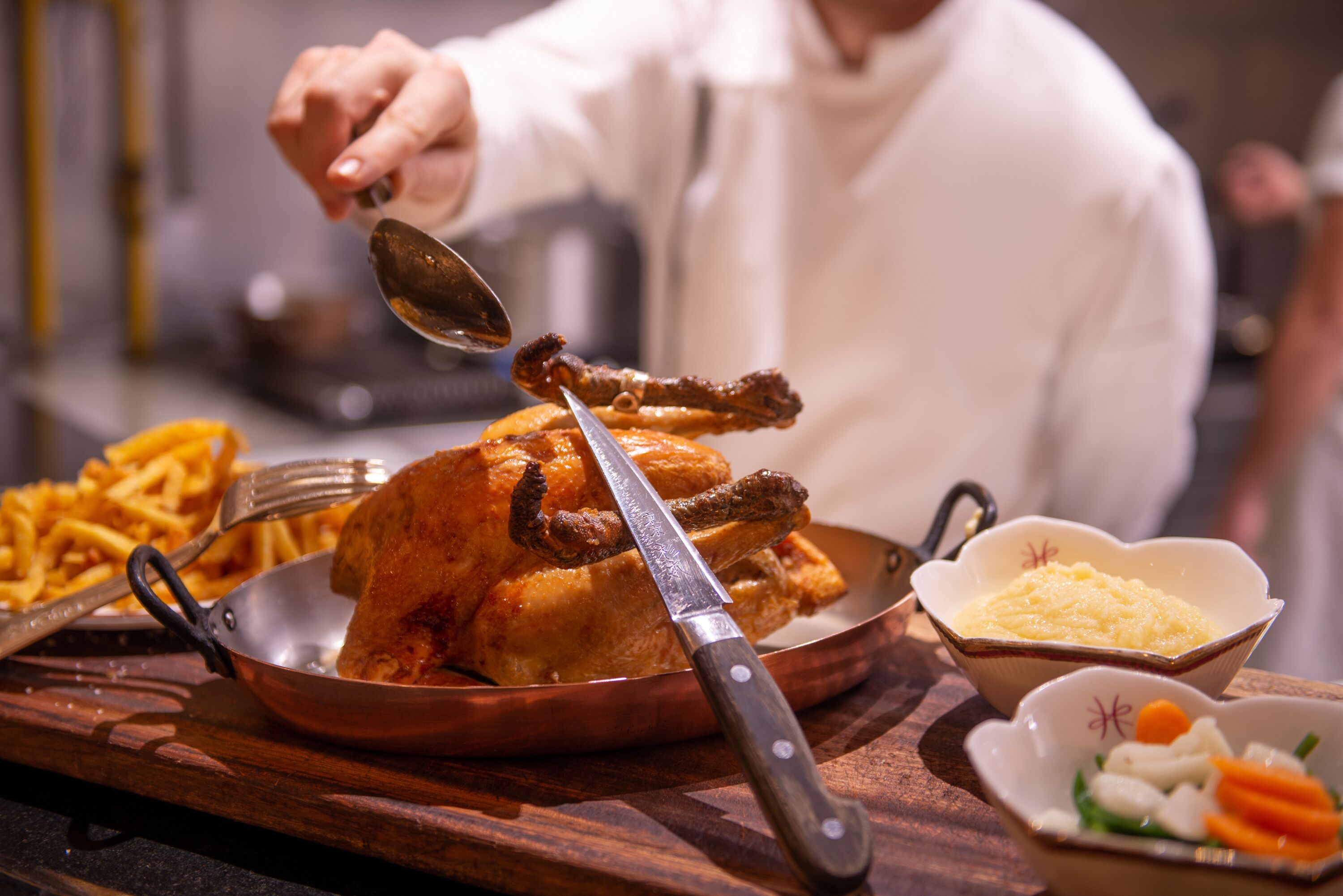 A roasted chicken with crispy skin, accompanied by French fries and a bowl of mashed potatoes.