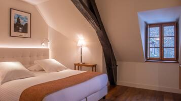 Un dormitorio con cama, mesita de noche, lámpara, un cuadro en la pared y ventana con vistas.