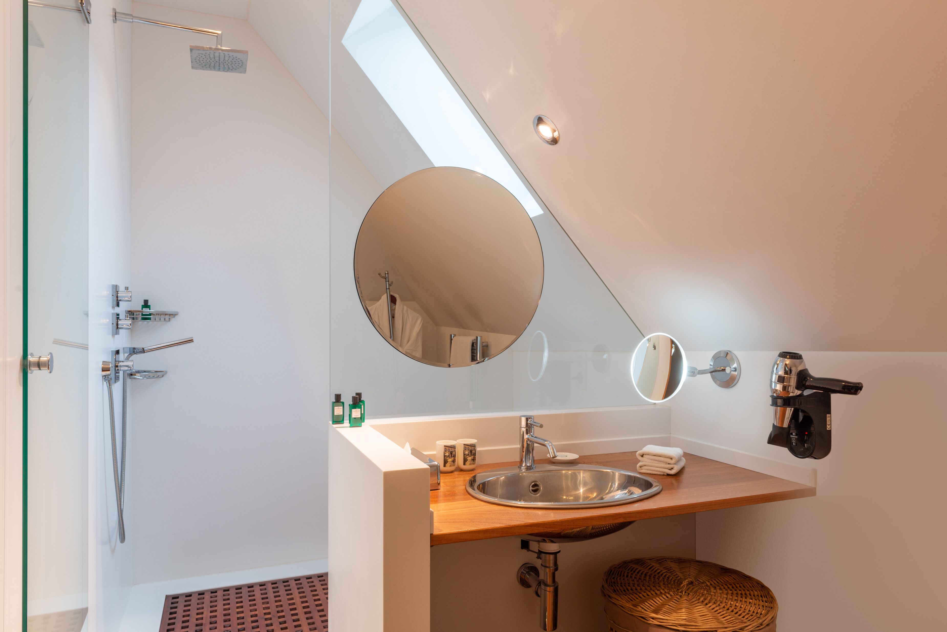 A modern bathroom with a skylight, a round mirror, a sink, and a shower.