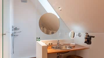 A modern bathroom with a skylight, a round mirror, a sink, and a shower.
