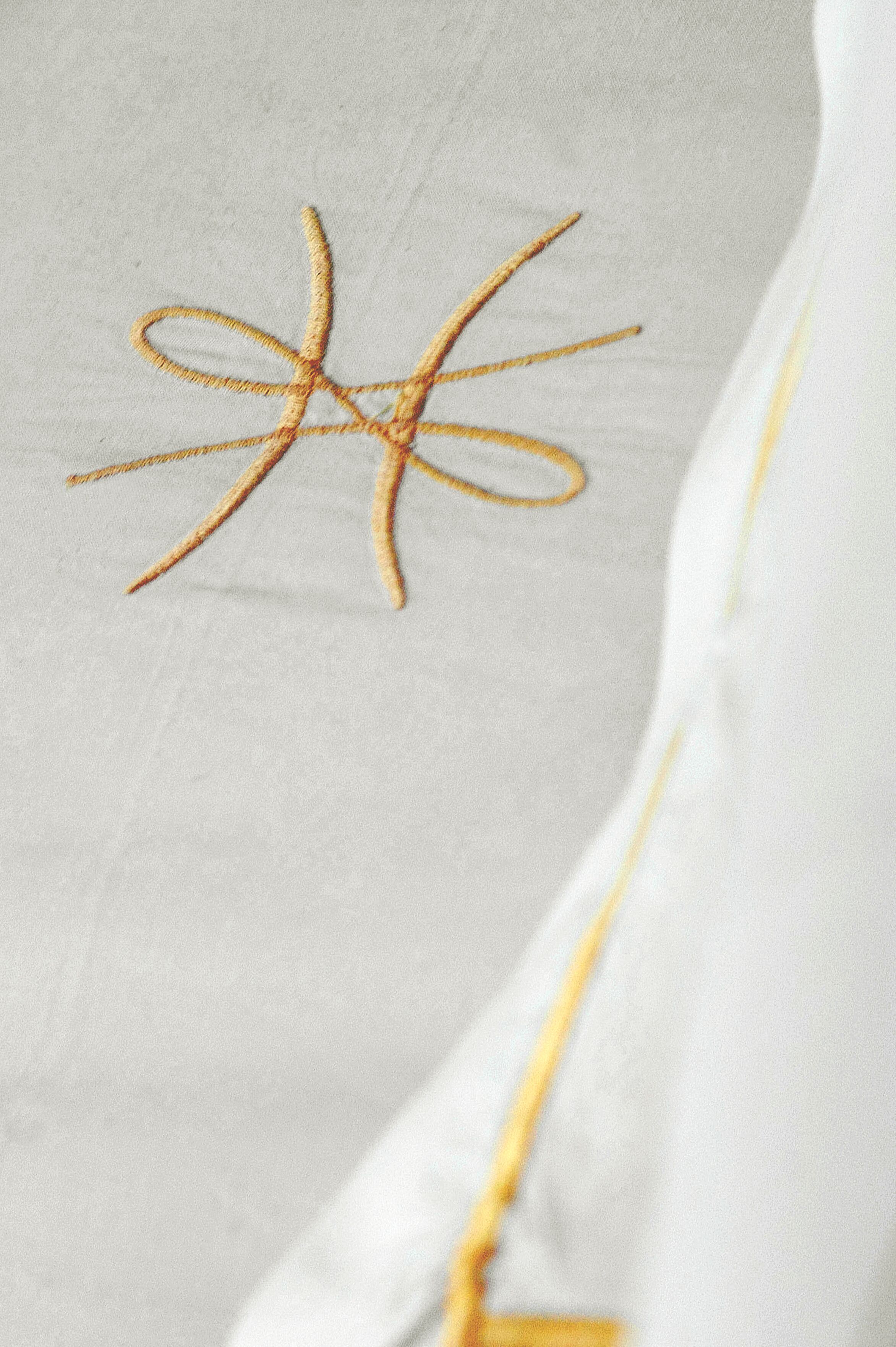 A close-up of a white fabric with a golden embroidered cross.