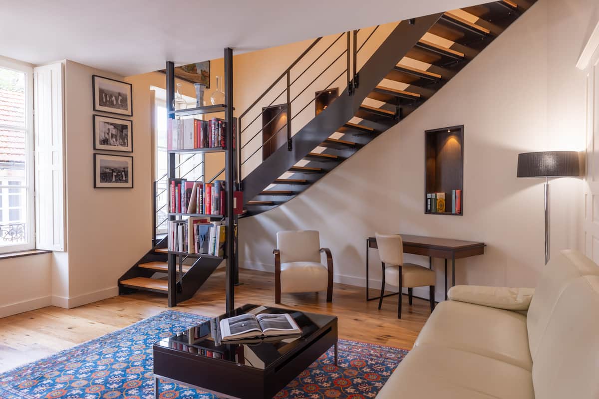 A modern living room with a staircase, a bookshelf, a coffee table, and a sofa.