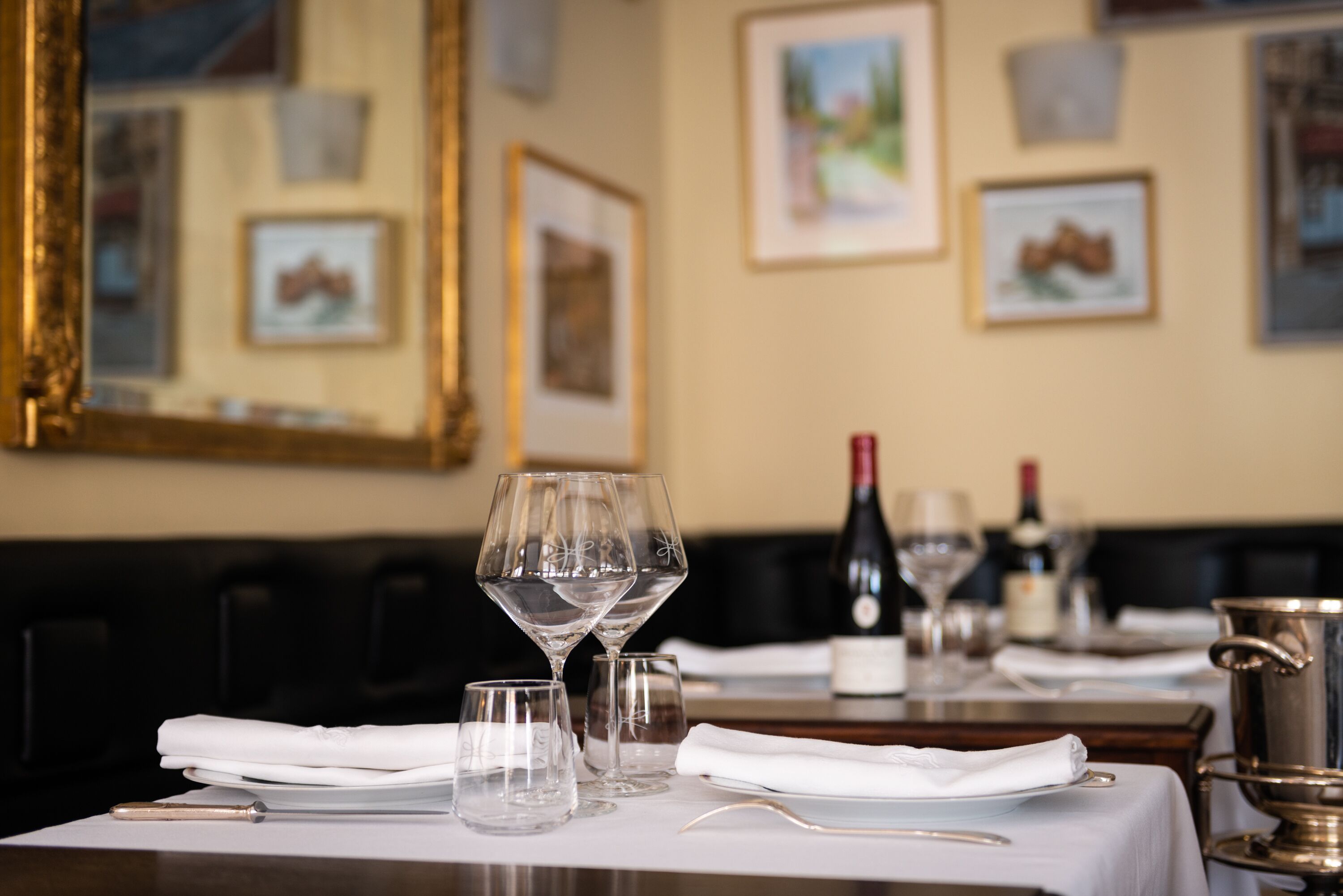 A dining table set with wine glasses, a bottle, and a silver pot.