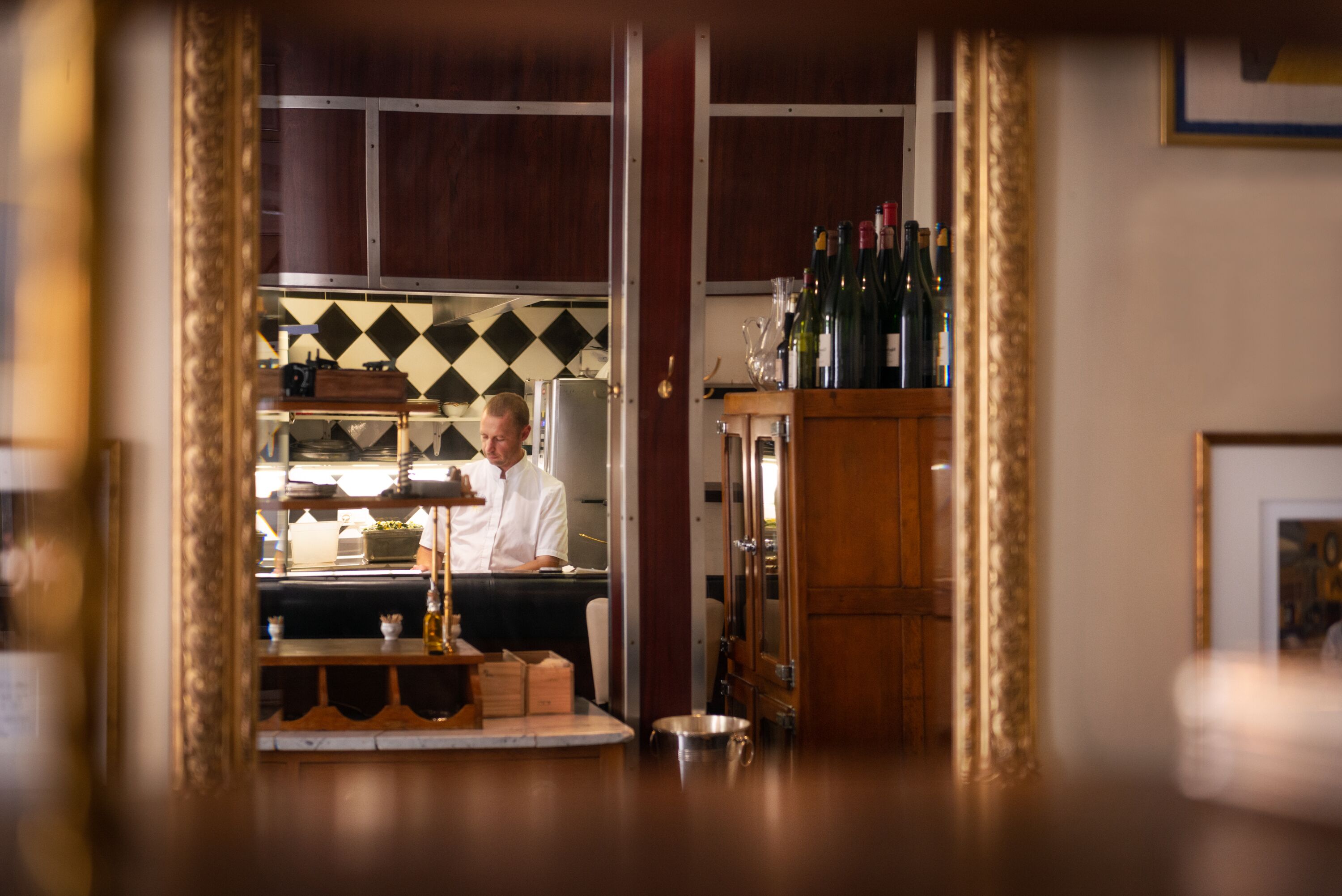 A bar area with a counter, bottles, and a refrigerator.