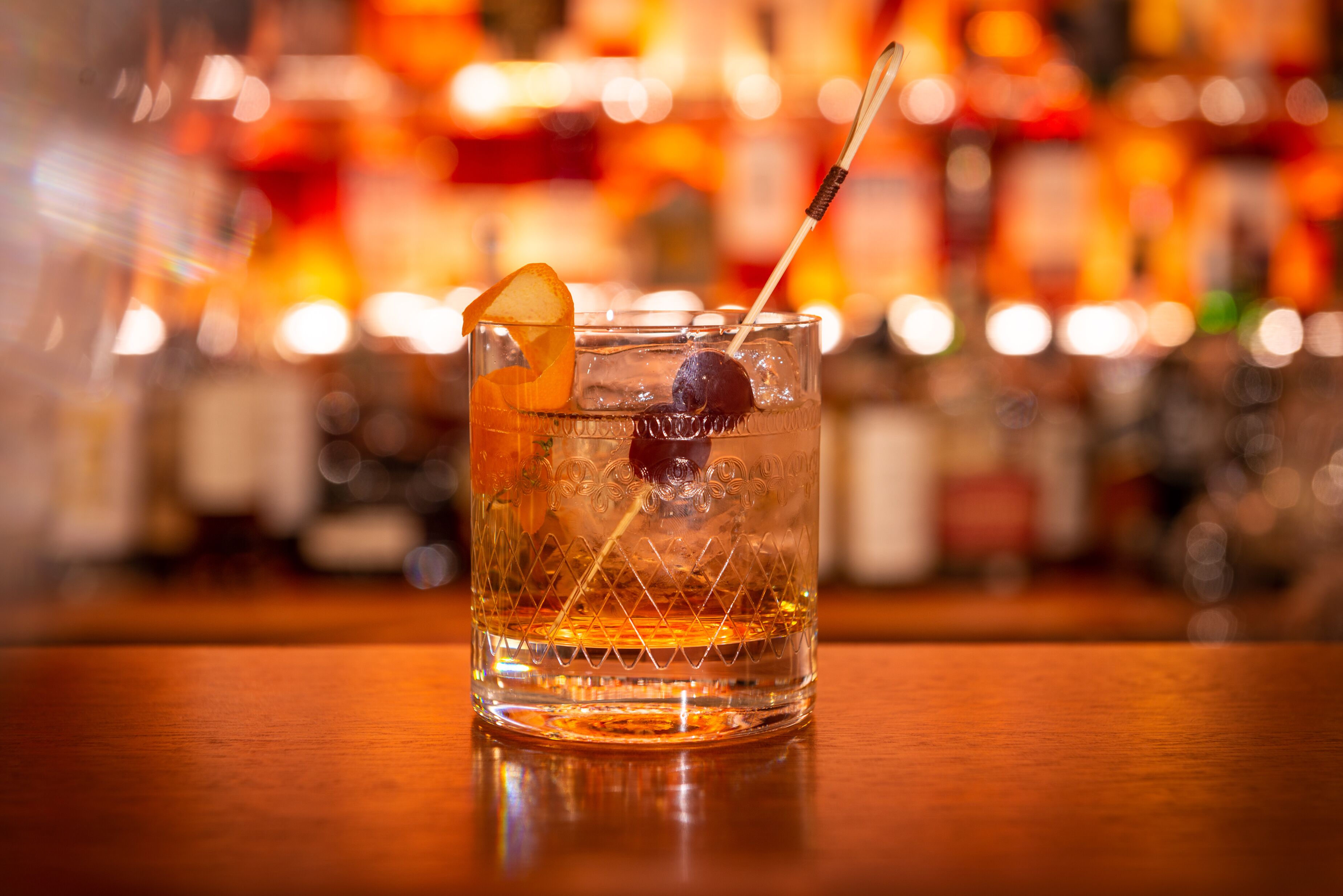 A clear glass with a cherry and an orange slice garnish, placed on a wooden surface.
