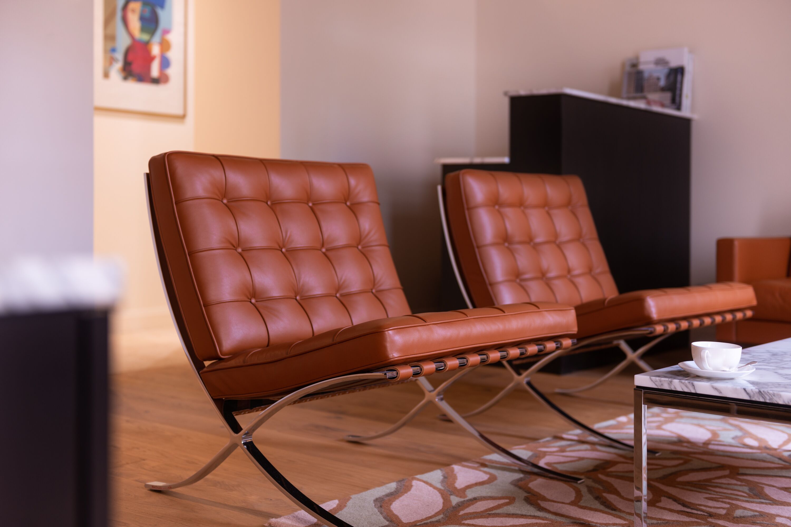 Two brown leather chairs with metal frames in a room with a wooden floor and a patterned rug.