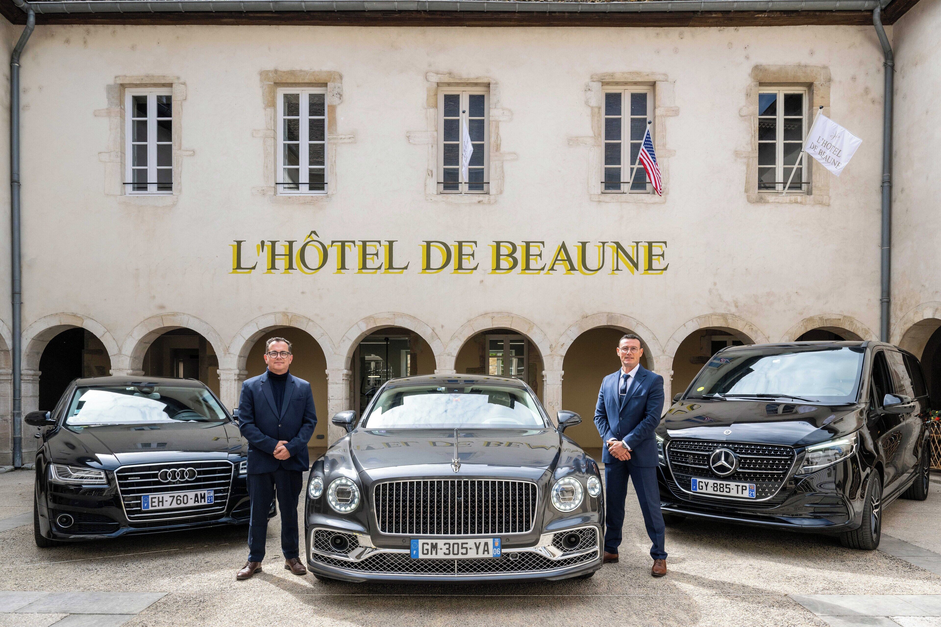 A building with the sign "L'Hôtel de Beaune" and two luxury cars parked in front.