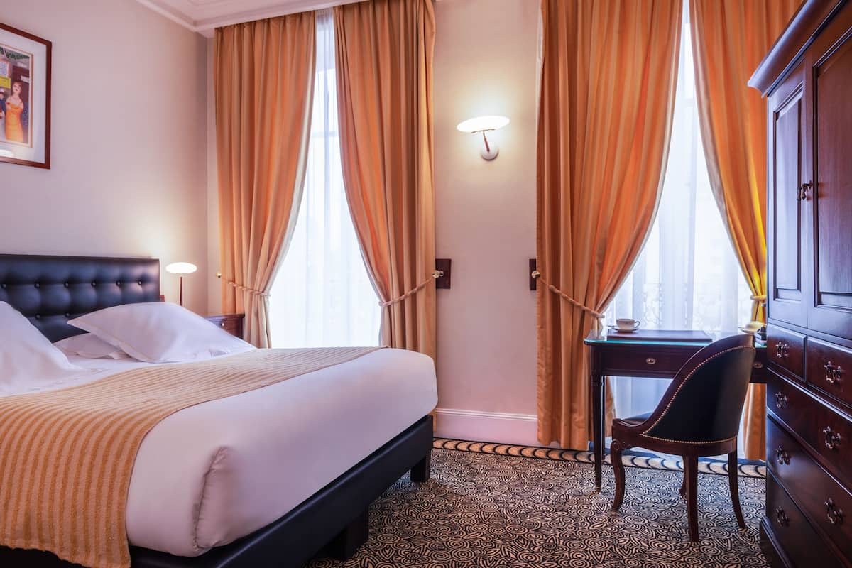 A hotel room with a large bed, a desk, and a wardrobe.