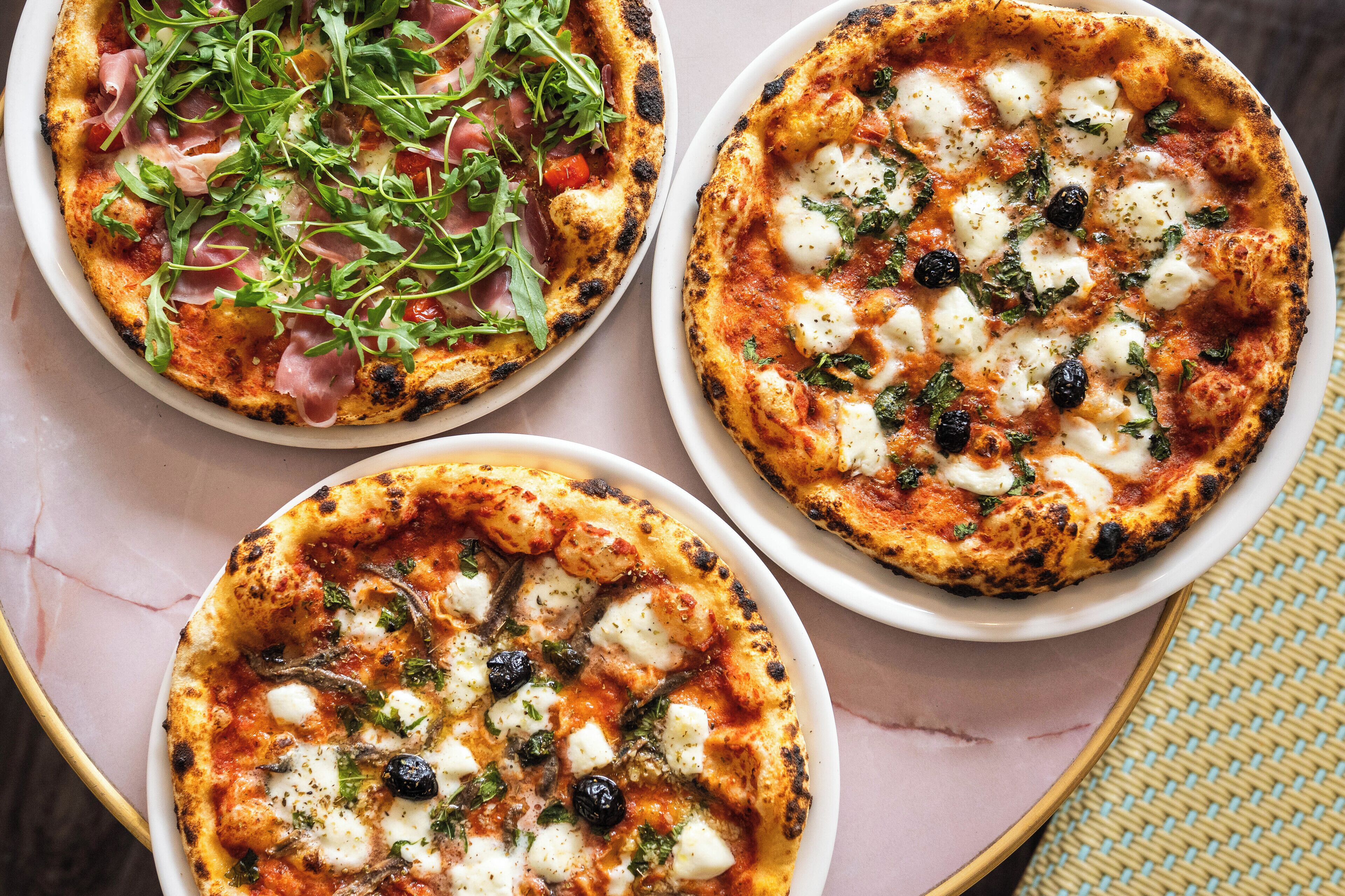 Three pizzas with different toppings on white plates.