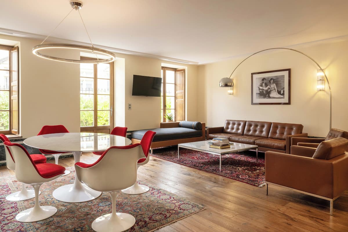 A modern living room with a round table, red and white chairs, a brown leather sofa, and a patterned rug.